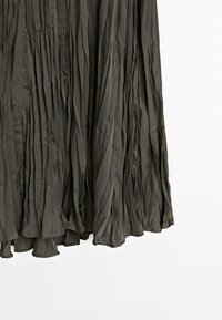 Plisowana maksisukienka w ciemnooliwkowym kolorze, wykonana z miękkiej, teksturowanej tkaniny. Charakteryzuje się zwiewnym krojem z falbanistym dołem.
