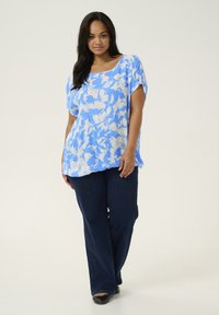 Light blue floral top with short sleeves, loose fit; paired with dark blue flared jeans and black flats. Smooth fabric texture.