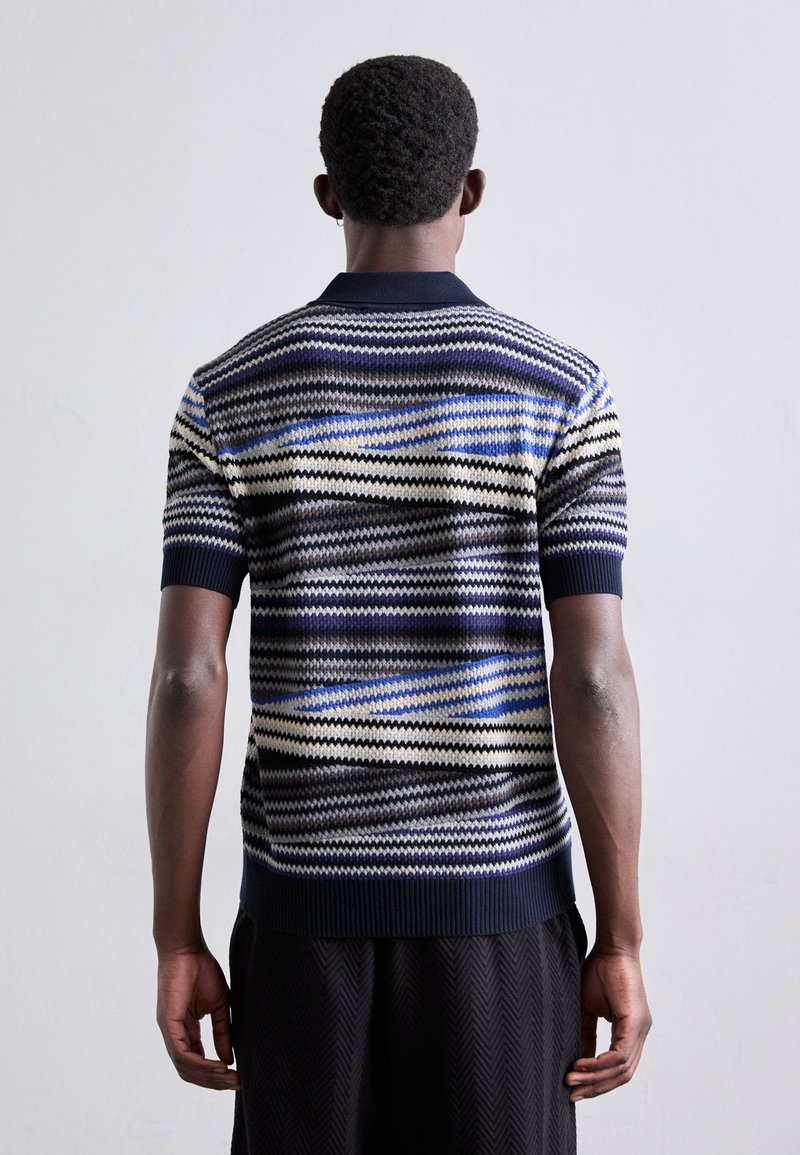 Polo shirt a maniche corte in maglia, con strisce blu, nere e crema. Presenta un colletto e un orlo a coste, con un motivo zigzag texture.
