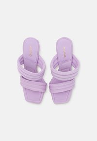 Lila klacksandaler med tre vadderade remmar, fyrkantig tå och en enkel pull-on design. Materialet verkar vara mjukt tyg med sömmar.