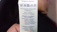 Rõivaste hooldusmärgise pesu sümbolid, tootja Saksamaalt, valmistatud Pakistanis, kangakoostisosade kirjeldus mitmes keeles, hoiab käes.