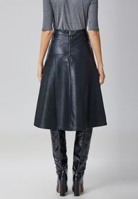 Jupe A-line en cuir noir avec une taille haute et une fermeture éclair dissimulée au dos. Texture lisse avec une forme structurée et évasée.