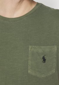 Olivově zelené bavlněné tričko s kulatým výstřihem, s náprsní kapsou a malým černým vyšívaným logem polo hráče na kapse.