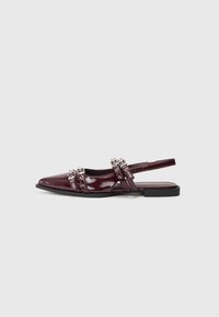Chaussure plate slingback en cuir verni bordeaux avec un bout pointu, présentant des lanières décoratives avec des accents métalliques.
