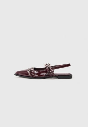 Chaussure plate slingback en cuir verni bordeaux avec un bout pointu, présentant des lanières décoratives avec des accents métalliques.