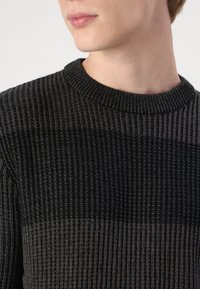 Maglione grigio lavorato a maglia con texture a costine, caratterizzato da strisce orizzontali contrastanti in diverse tonalità di grigio e un collo rotondo.
