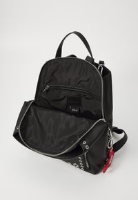 Zaino in pelle nera con cerniere argentate, una tasca interna con zip e una texture liscia. Presenta un portachiavi rosso e dettagli metallici.