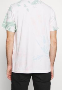 T-shirt di cotone bianco con un motivo tie-dye verde e rosa, maniche corte, vestibilità standard e scollo a girocollo.