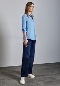Camicia azzurra a righe, jeans larghi blu scuro e sneakers bianche. Tessuto morbido, vestibilità rilassata, maniche arrotolate e design minimal.