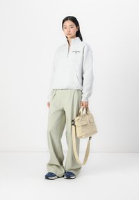 Sweat-shirt zippé gris clair avec poches frontales, associé à un pantalon olive à jambes larges. Comprend un petit sac beige avec deux poches avant.