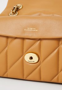 Tabby-väska i äkta nappa-läder i tan, med en quiltad design, gyllene metalldetaljer och präglad logotyp på framsidan.