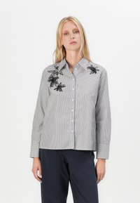 Stripete skjorte med lange ermer, med svarte broderte blomsterdetaljer på venstre side og rett kutt i hemline.
