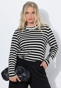 Zwart-wit gestreepte lange mouw top met een hoge kraag, gecombineerd met zwarte broek. Een zwarte leren clutch wordt in één hand vastgehouden.