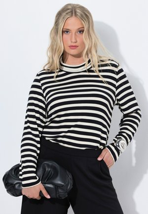 Zwart-wit gestreepte lange mouw top met een hoge kraag, gecombineerd met zwarte broek. Een zwarte leren clutch wordt in één hand vastgehouden.