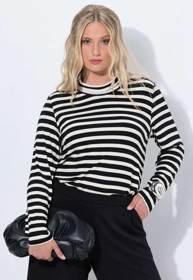 Zwart-wit gestreepte lange mouw top met een hoge kraag, gecombineerd met zwarte broek. Een zwarte leren clutch wordt in één hand vastgehouden.