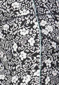 Svart och vit blommönstrad textil med sömnad och en tunn ljusblå vertikal sömdetalj.