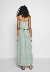 Robe maxi verte à pois blancs, avec une taille cintrée et des bretelles fines. Tissu léger avec une silhouette fluide.