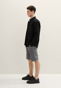 Black long-sleeve shirt, gray cargo shorts, and black sneakers worn by a person standing sideways against a neutral background.