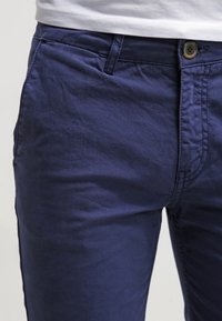 Navy blue cotton-chino pants with a smooth texture, slim fit, front pockets, and a button closure detail.