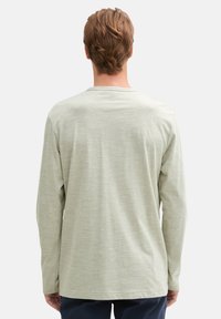 Helles grünes langärmliges T-Shirt aus weichem Stoff, mit Rundhalsausschnitt und subtilem Strukturmuster. Schlichtes, lässiges Design.