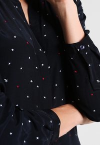 Navy blouse featuring white, red, and blue star patterns; long sleeves with button cuffs; soft, textured fabric; casual collar design.