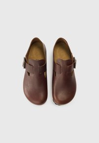 Bruine leren klompen met een gestructureerde afwerking, afgeronde vorm, uitgesneden details en een zijkant gesp sluiting. Zachte binnenzolen en platte zolen.