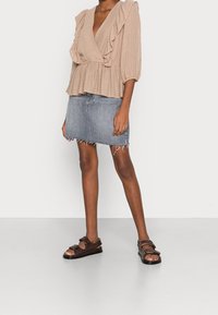 Beige stribet peplum top med flæser, parret med en frayed denimskørt og brune læderrem sandaler med spænde detaljer.