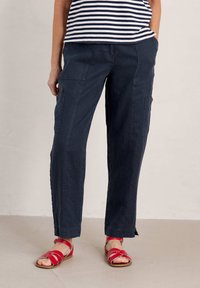 Navy cargo pants with a relaxed fit, featuring side pockets and a subtle texture. Worn with red strappy sandals on a neutral floor.