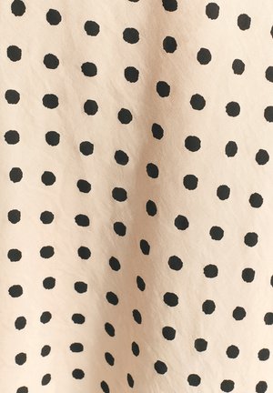 Hellbeiger Stoff mit über das gesamte Muster gleichmäßig verteilten schwarzen Polka-Dots, die in Größe und Form leicht variieren.