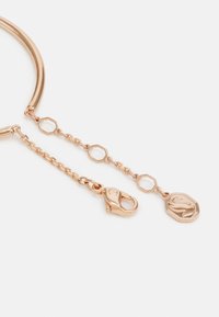 Armband aus Roségold mit einem glatten, runden Band, einer dekorativen Kette mit hexagonalen Gliedern, einem Karabinerverschluss und einem geprägten Anhänger.