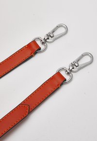 Deux sangles en cuir orange avec des fermoirs pivotants en métal argenté attachés à des anneaux métalliques ronds sur un fond blanc uni.