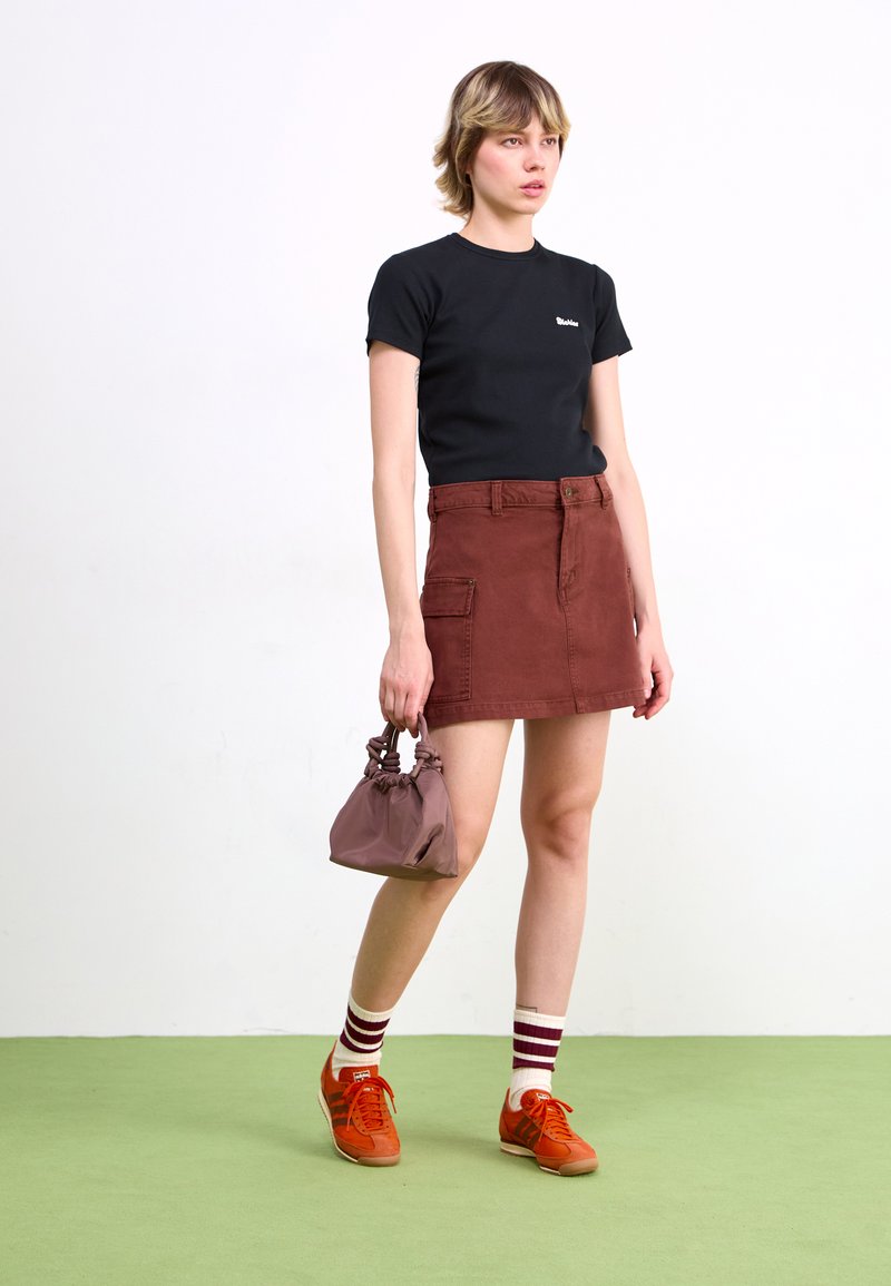 Camiseta negra de manga corta, falda de mezclilla color óxido y zapatillas naranjas. Presenta un mini bolso marrón y calcetines a rayas. Elementos de diseño simples.