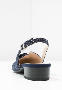 Zapato de tacón de ante azul marino con correa de lunares y hebilla, diseño de espalda abierta y tacón grueso negro. Forro interior suave.