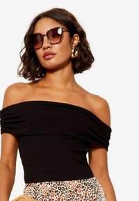 Juodas off-the-shoulder raštuotas viršus su trumpomis rankovėmis, derinamas su gepardo rašto sijonu. Modelis dėvi dideles tamsias saulės akinius ir auksines auskarus-žiedus.