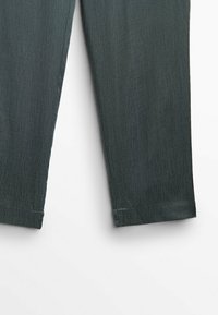 Pantalons en denim vert foncé avec une texture lisse et des jambes étroites. Les ourlets sont légèrement retroussés avec des coutures soignées et sans matériel visible.