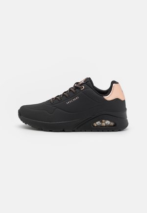 Zwarte Skechers sneaker met roségouden hieldetail, luchtgeveerde zool en zwarte en roségouden veters, zijaanzicht op witte achtergrond.