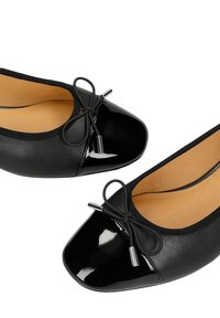 Czarne baleriny z błyszczącymi lakierowanymi noskami, małymi dekoracyjnymi kokardkami i beżowymi wyściółkami, pokazane z góry.