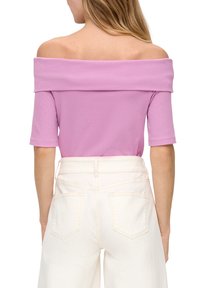 Top bez ramienok v lila farbe s krátkymi rukávmi, hladký textil, nosený s bielymi nohavicami s vysokým pásom, ktoré majú zadné vrecká a detaily šitia.