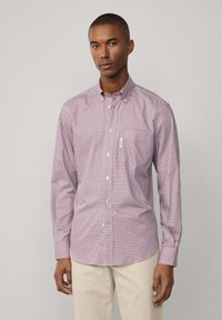Camicia da uomo a maniche lunghe con bottoni, in un motivo a quadri rosso e bianco, dotata di colletto a punta e taschino sul petto, abbinata a pantaloni beige.