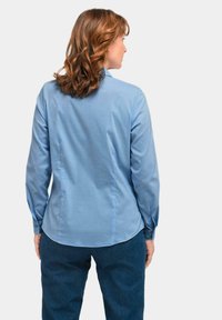 Hellblaues Hemd mit langen Ärmeln, abgerundetem Saum und glatter Textur. Kombiniert mit dunkelblauen Jeans.