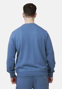 Felpa blu con maniche lunghe, polsini e orlo a costine, e scollatura a girocollo. Realizzata in un tessuto morbido con una superficie liscia.