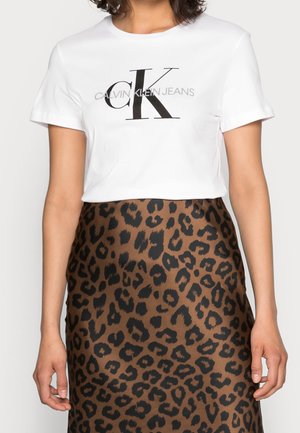 T-shirt blanc à manches courtes Calvin Klein Jeans avec un grand logo noir, associé à une jupe imprimé léopard marron et noir.
