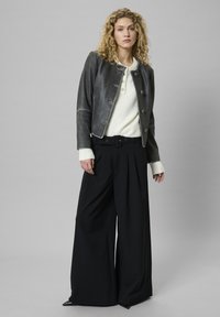 Szürke bőrkabát, rövidített fazonnal, kerek gallérral és gombos záródással; egy törtfehér pulóverrel és fekete, bőszárú nadrággal párosítva.