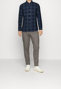 Laivastonsininen ruudullinen napillinen paita yhdistettynä vaaleanharmaisiin housuihin ja valkoisiin lenkkareihin. Paidassa on kaulus ja näkyvät napit.