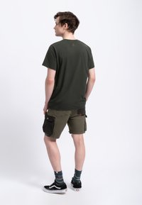 Olijfgroen t-shirt met ronde hals, gecombineerd met khaki shorts met zwarte accenten en zakken, afgemaakt met zwarte sneakers en gestreepte sokken.