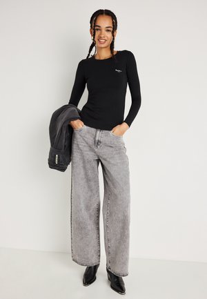 Svart långärmad topp, ljusgrå vida jeans, svarta spetsiga ankelstövlar och en grå jacka slängd över vänster arm. Minimalistiska stil detaljer.