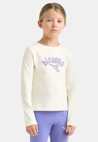 Maglietta a maniche lunghe color crema con la scritta "DIADORA" in viola, abbinata a leggings viola chiaro. Tessuto liscio, design aderente, senza motivi visibili.