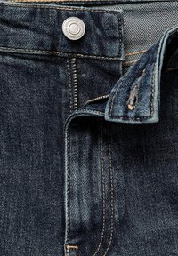 Jean en denim bleu foncé avec une fermeture éclair partiellement ouverte et un bouton argenté à la taille.