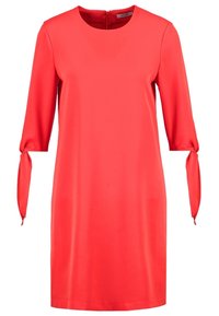 Robe rouge longueur genoux avec manches trois-quarts, col rond et liens aux poignets.