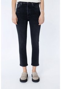Jeans de mezclilla negros de tiro alto, con un corte recto, longitud recortada y dobladillo sin rematar. Combinados con mocasines marrones con un detalle de flecos.